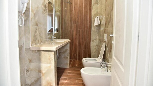 Un baño con pared de mármol, panel de madera, lavamanos, inodoro y bidé.