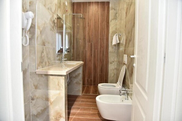 Un baño con pared de mármol, panel de madera, lavamanos, inodoro y bidé.