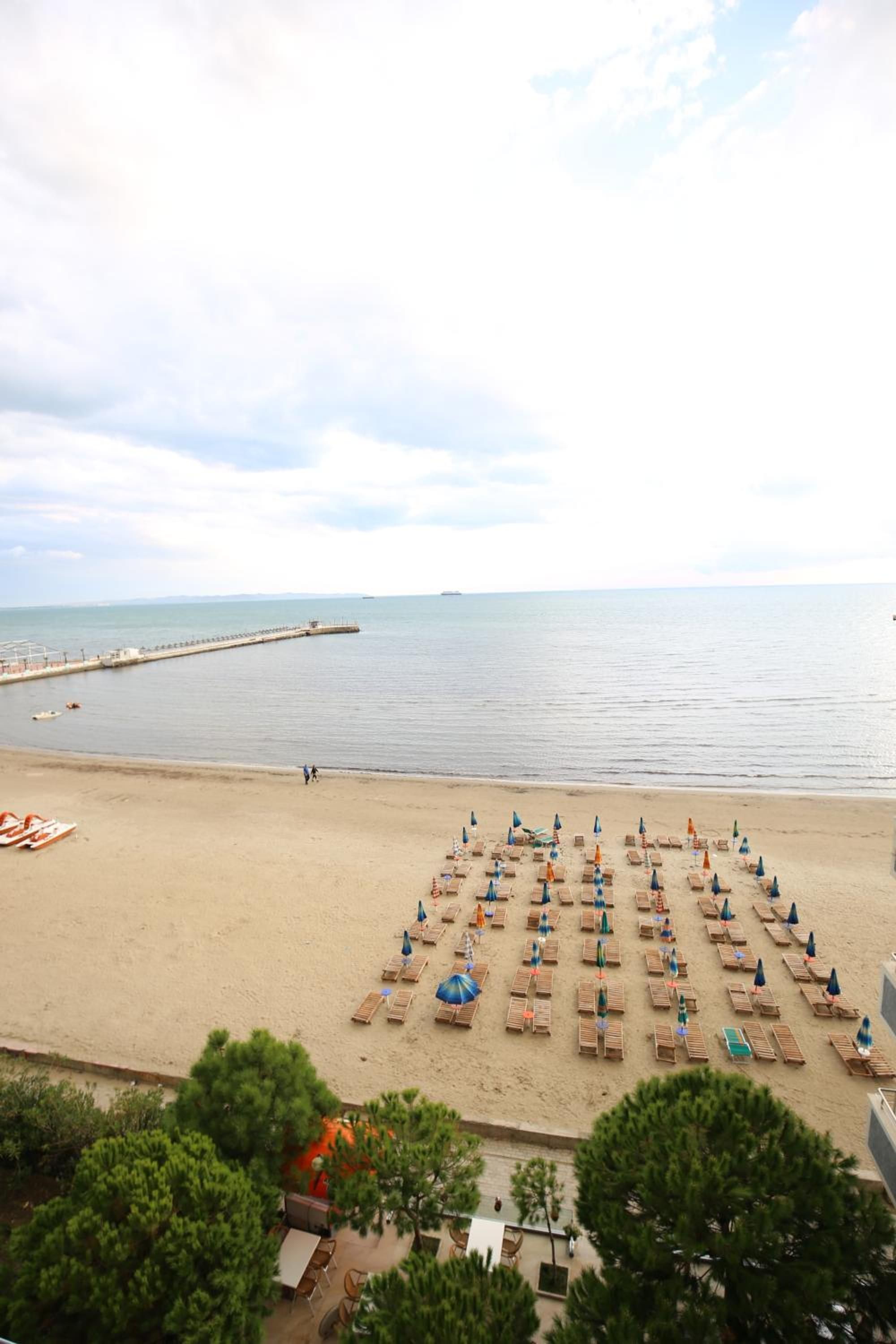 A beach with rows of sun loungers and umbrellas, a pier in the background, and a calm sea.