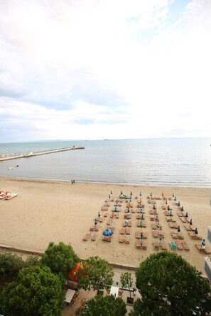 A beach with rows of sun loungers and umbrellas, a pier in the background, and a calm sea.