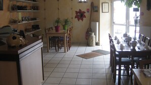 Un coin repas avec une longue table dressée pour le repas, des chaises, une plante en pot et un extincteur.