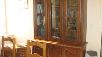 Une bibliothèque en bois avec des portes en verre, une chaise en bois et une petite table recouverte d’une nappe rouge.