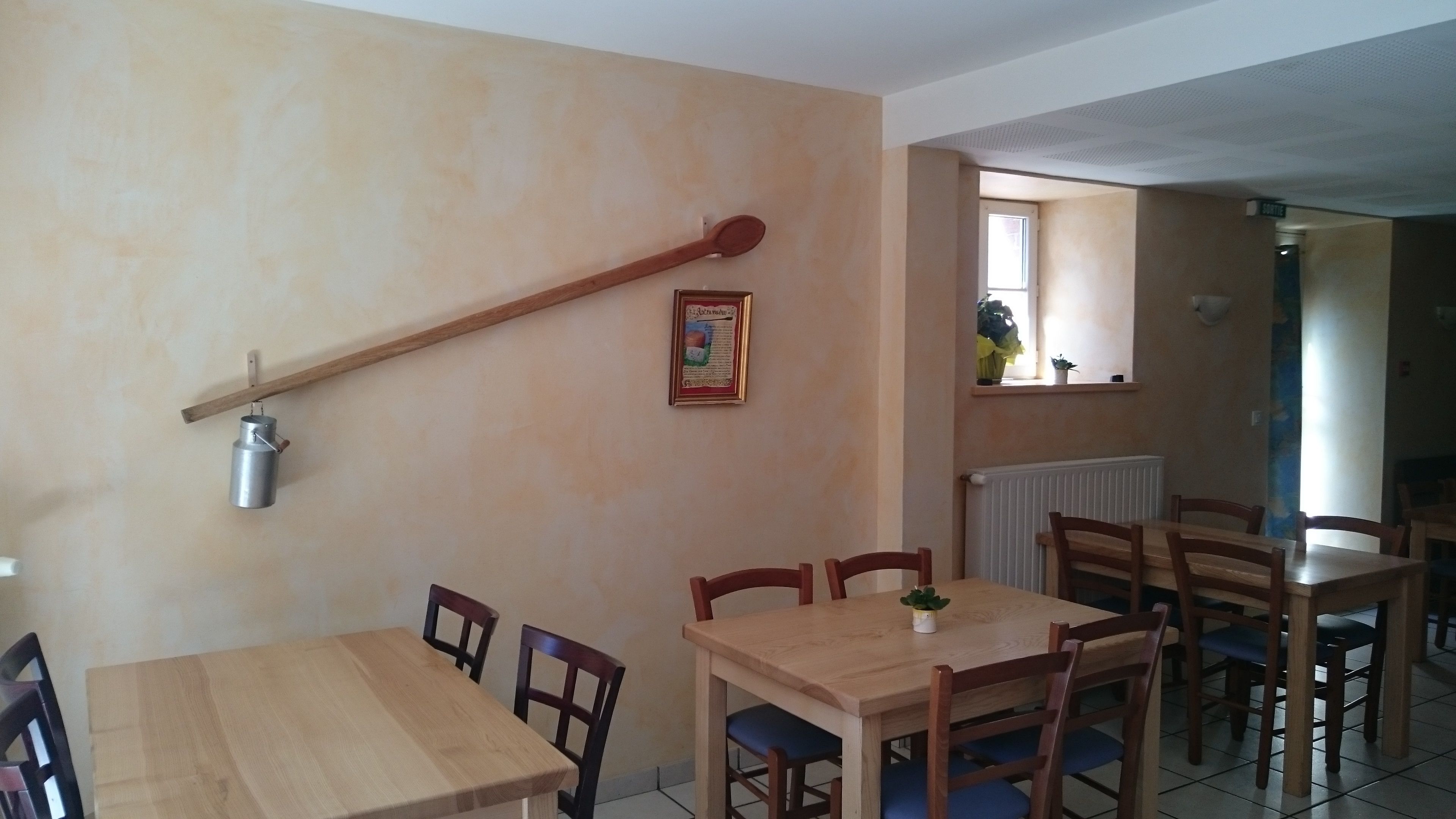 A dining area with wooden tables and chairs, a hanging metal container, and a framed certificate on the wall.