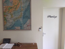 Un mapa en la pared, una puerta con la etiqueta "Planée" y un escritorio de madera con una pizarra y utensilios de escritura.