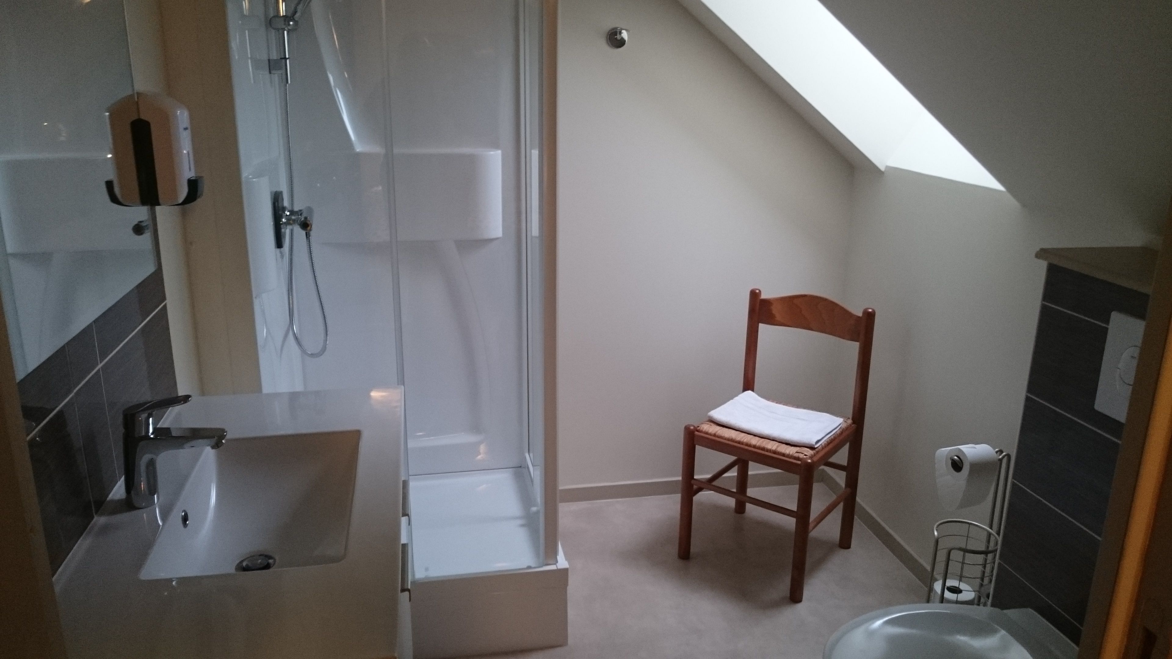 A small, modern bathroom with a shower, a sink, and a wooden chair.