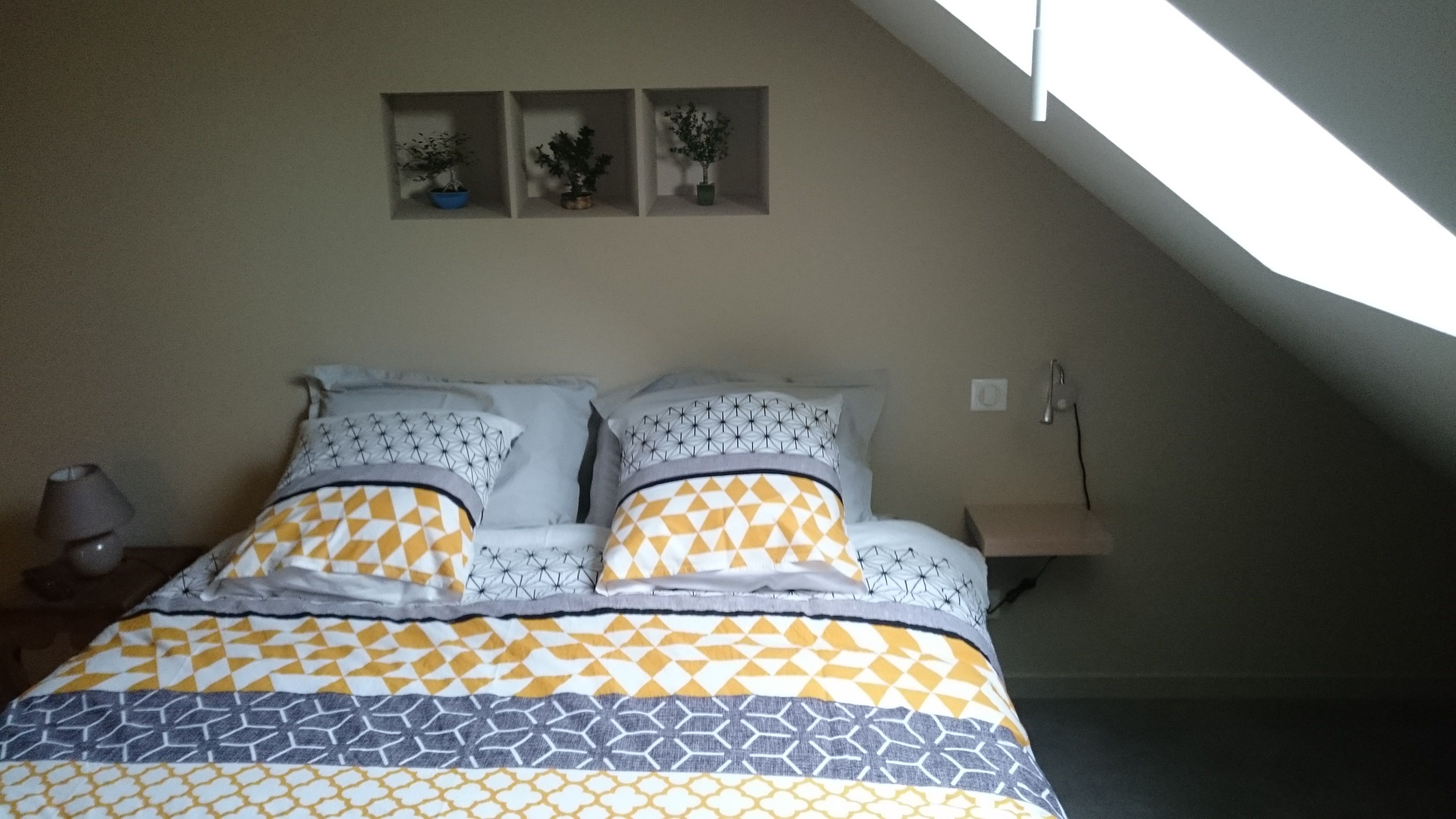 Une chambre à coucher avec un lit, une table de chevet, une lampe et une petite table sur laquelle est posée une plante.