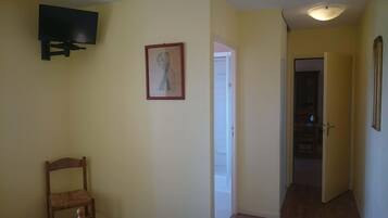 Een gang met een houten stoel, een ingelijst kunstwerk aan de muur en een aan de muur bevestigde televisie.