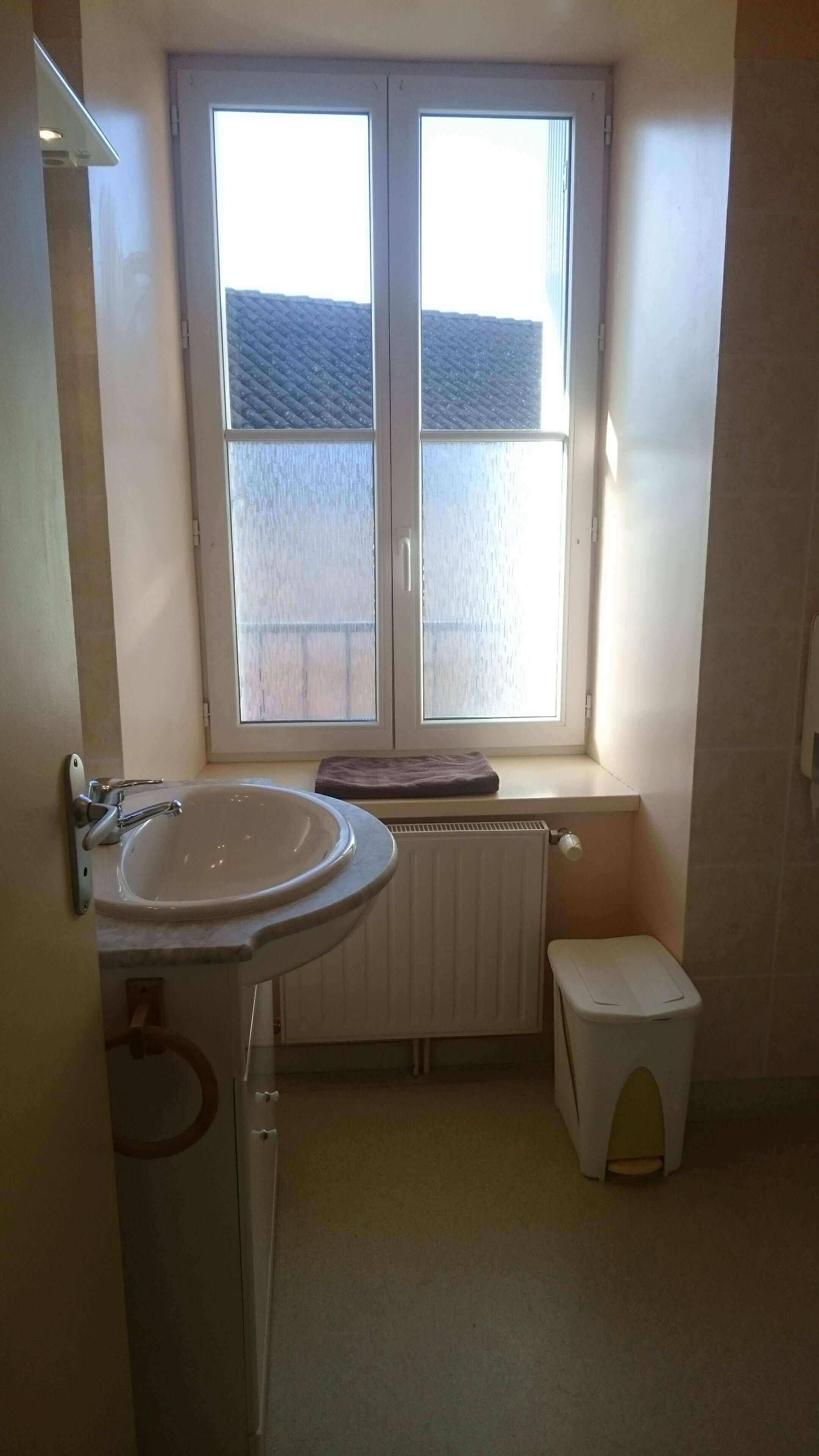 A small bathroom with a window, a sink, a toilet, and a radiator.
