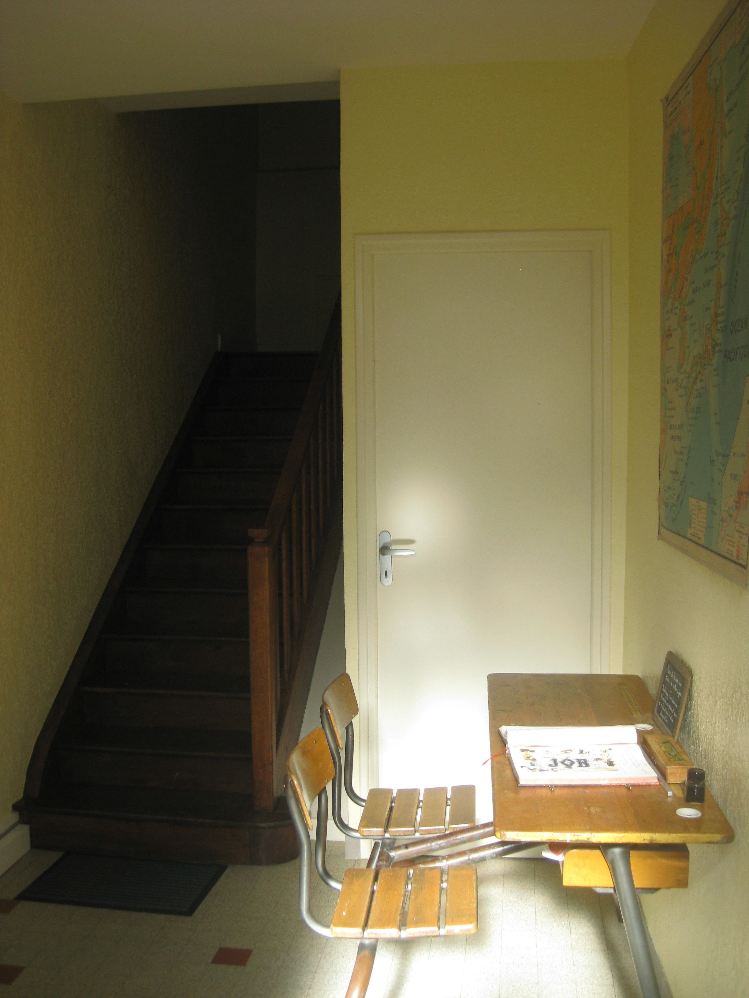 A room with a wooden table, two chairs, a map on the wall, and a staircase.