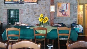 A dining area with stone walls, wooden chairs, a table with a green tablecloth, and a vase with sunflowers. - Agriturismo La Praduscella (Fivizzano)