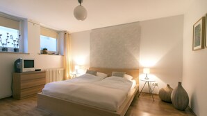 Ein modernes Schlafzimmer mit einem großen Bett, Nachttischlampen, einem Schminktisch, einem Fernseher und dekorativen Vasen.