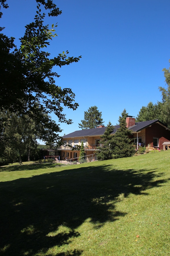 A residential property with a large lawn, a tennis court, and a house with a sloped roof.