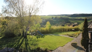 Ein Garten mit Schaukel und Rutsche, umgeben von viel Grün und Blick auf die Landschaft.