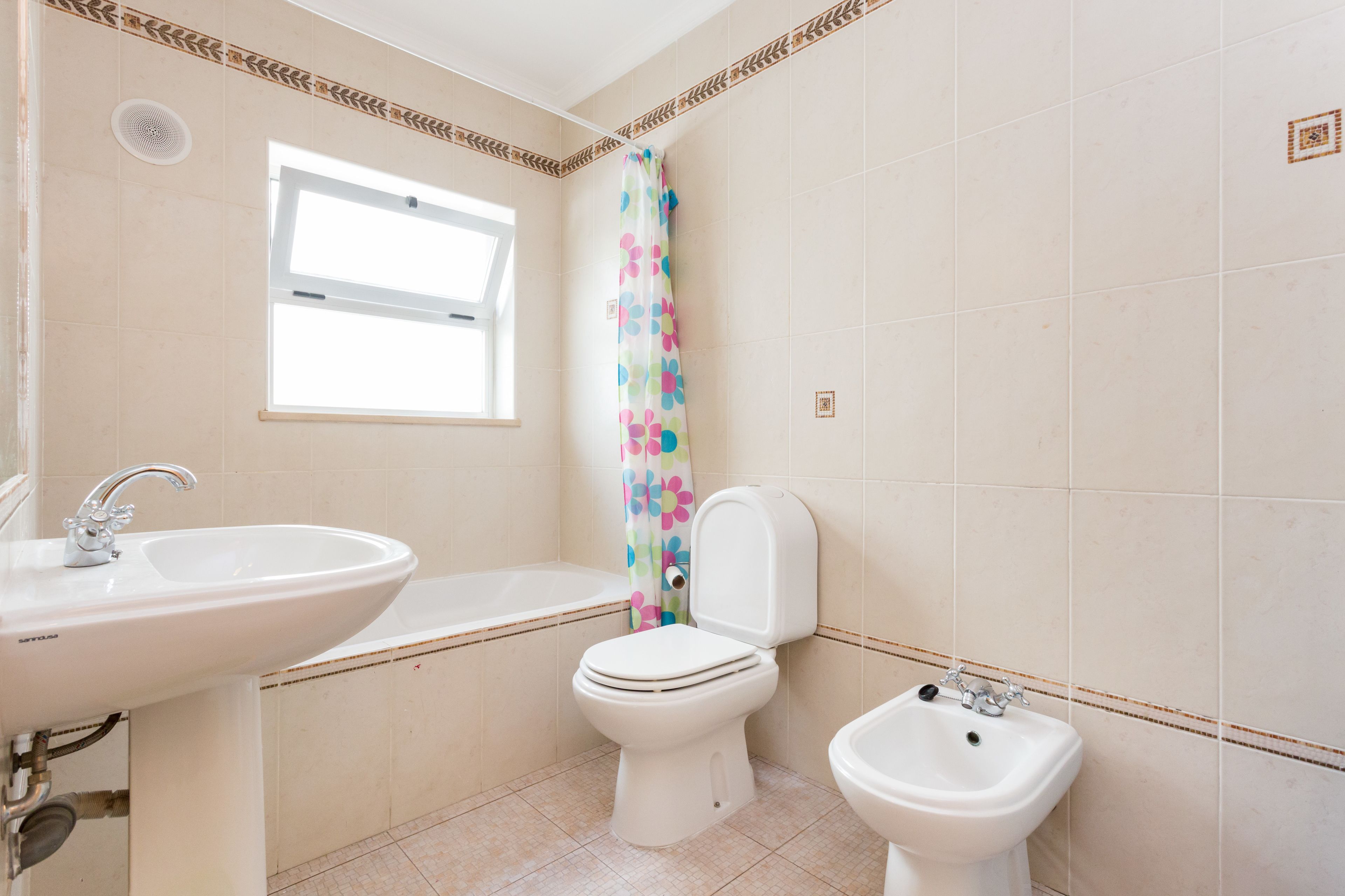 A bathroom with a sink, toilet, bidet, and a window.