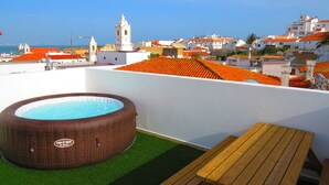 A rooftop terrace with a hot tub, a wooden table, and a view of the cityscape including a church tower. - The 17 Hostel (Lagos)