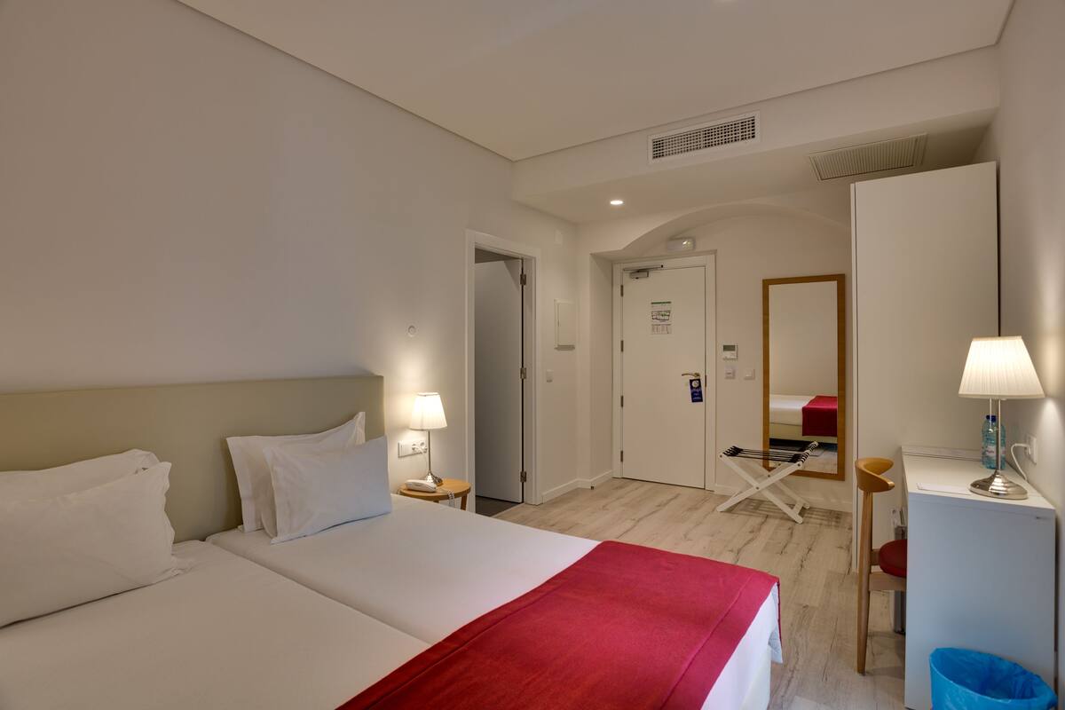 A hotel room with a large bed, a desk, a chair, a mirror, and a small trash bin.