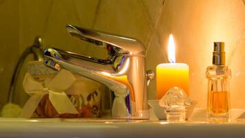 A bathroom sink with a modern faucet, a lit candle, and a bottle of liquid soap.