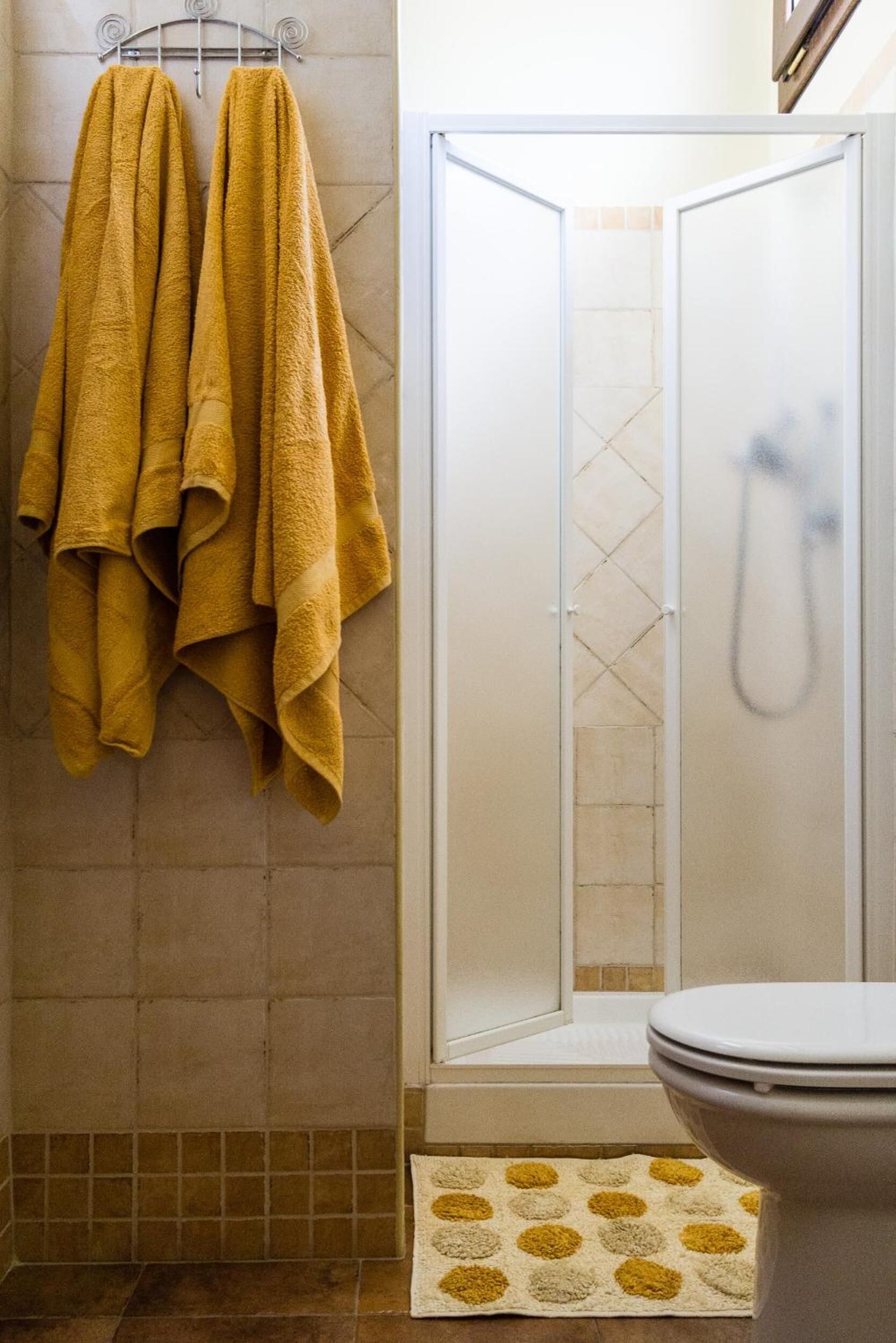 Un bagno con cabina doccia, un water e un portaservizi con asciugamani gialli.