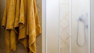 Un bagno con cabina doccia, un water e un portaservizi con asciugamani gialli.