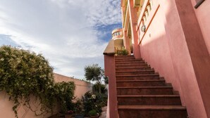 A staircase leading to a building with a pink facade and a garden area with potted plants. - B&B Su Connotu (Sestu)