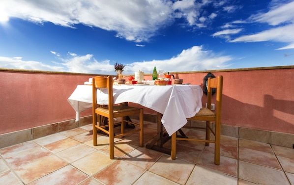 A terrace with a table set for two, chairs, a potted plant, and a decorative lantern.