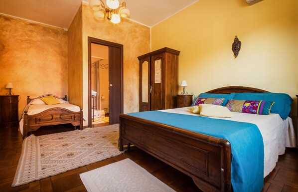 A bedroom with a wooden bed, a nightstand, a dresser, and a door leading to another room. - B&B Su Connotu (Sestu)