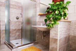 A modern bathroom with a glass shower enclosure, a sink, and a potted plant. - B&B Su Connotu (Sestu)