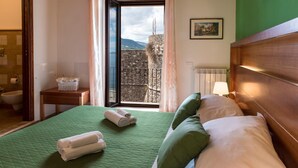 Habitación de hotel con edredón verde acolchado, cabecero de madera y vistas a una pared de piedra y montañas a través de un ventanal grande.