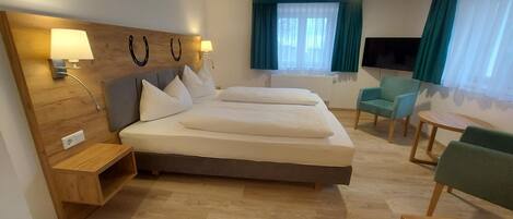 A hotel room with a large bed, two bedside tables, a desk, a chair, and a TV.
