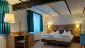 Un dormitorio con una cama doble, un escritorio con silla, una lámpara y un ventanal con cortinas.