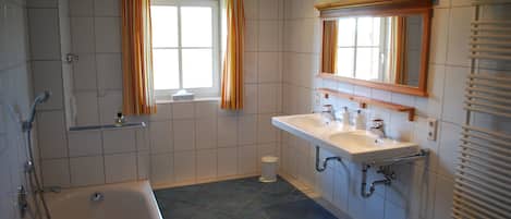 A bathroom with a bathtub, two sinks, a window with curtains, and a mirror above the sinks.