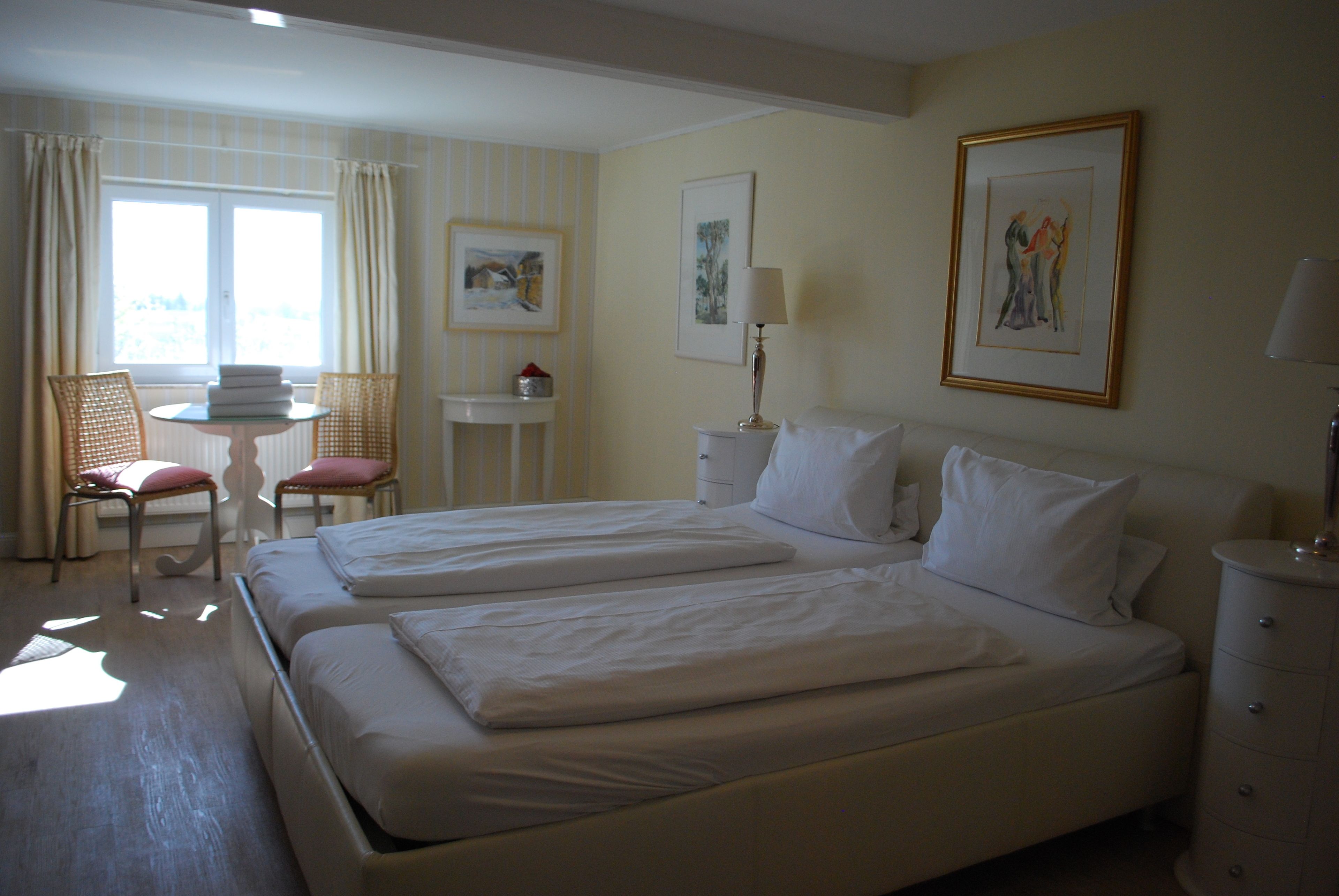 A hotel room with two beds, a small table, a chair, and a window with curtains.