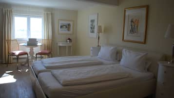 A hotel room with two beds, a small table, a chair, and a window with curtains.