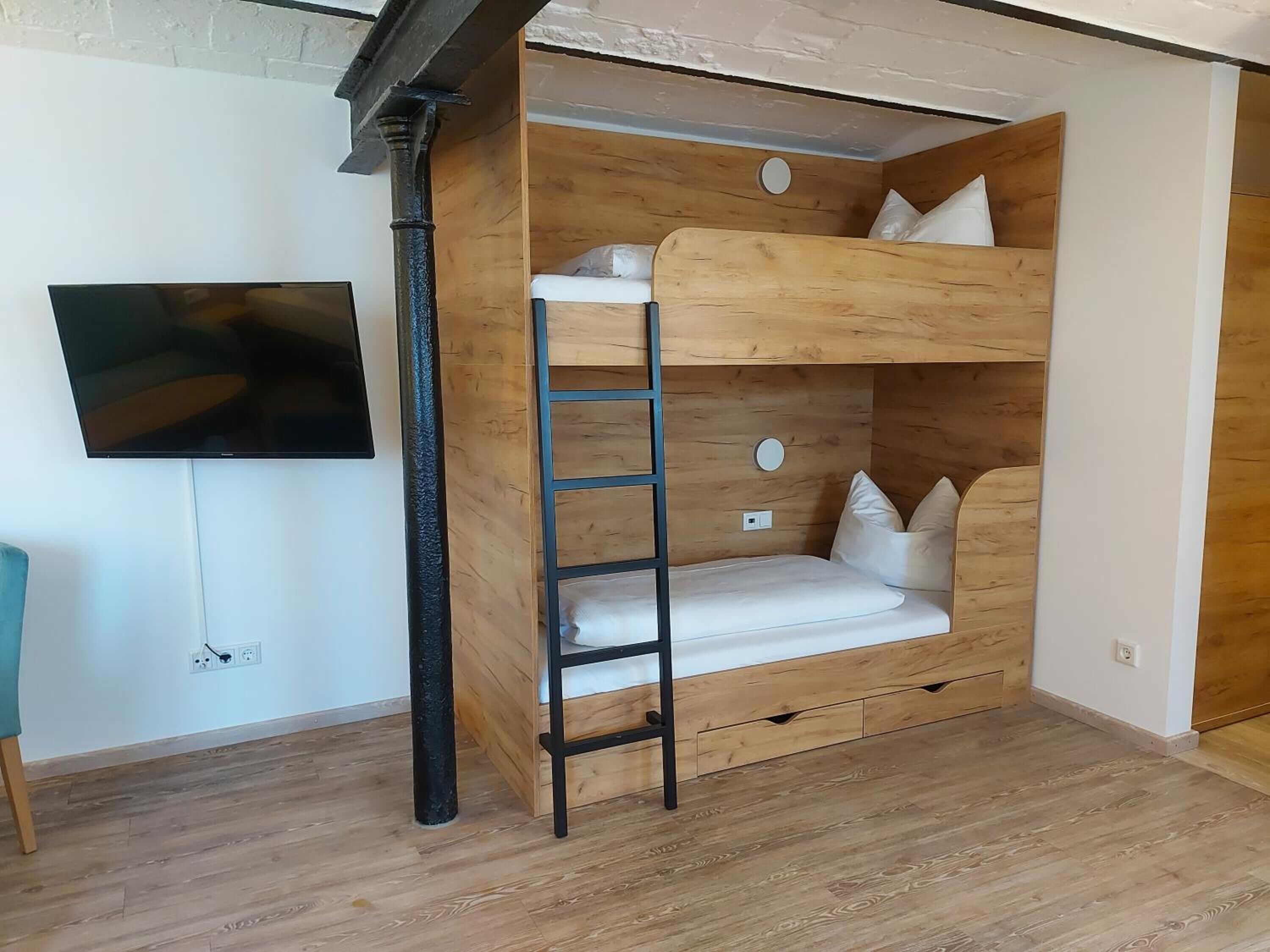 A bunk bed with a ladder, a TV mounted on the wall, and a wooden floor.