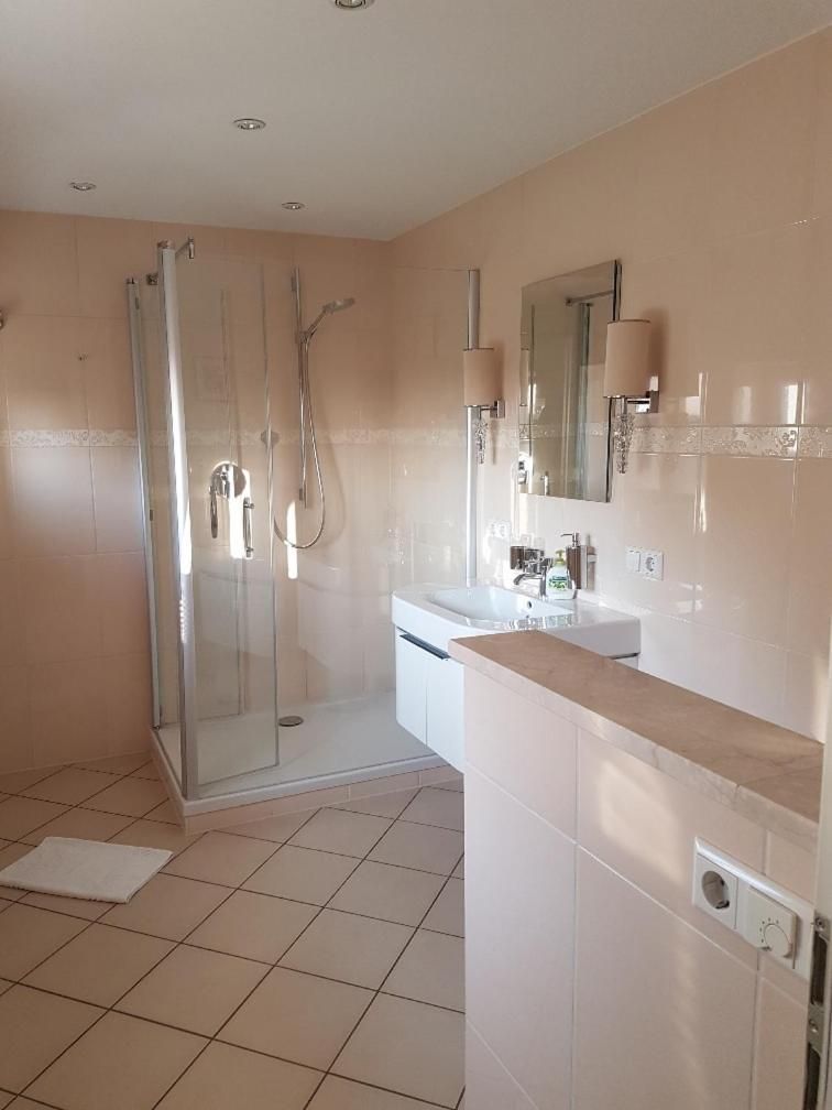 Een moderne badkamer met een douche in een glazen cabine, een witte wastafel en een spiegel boven het aanrecht.