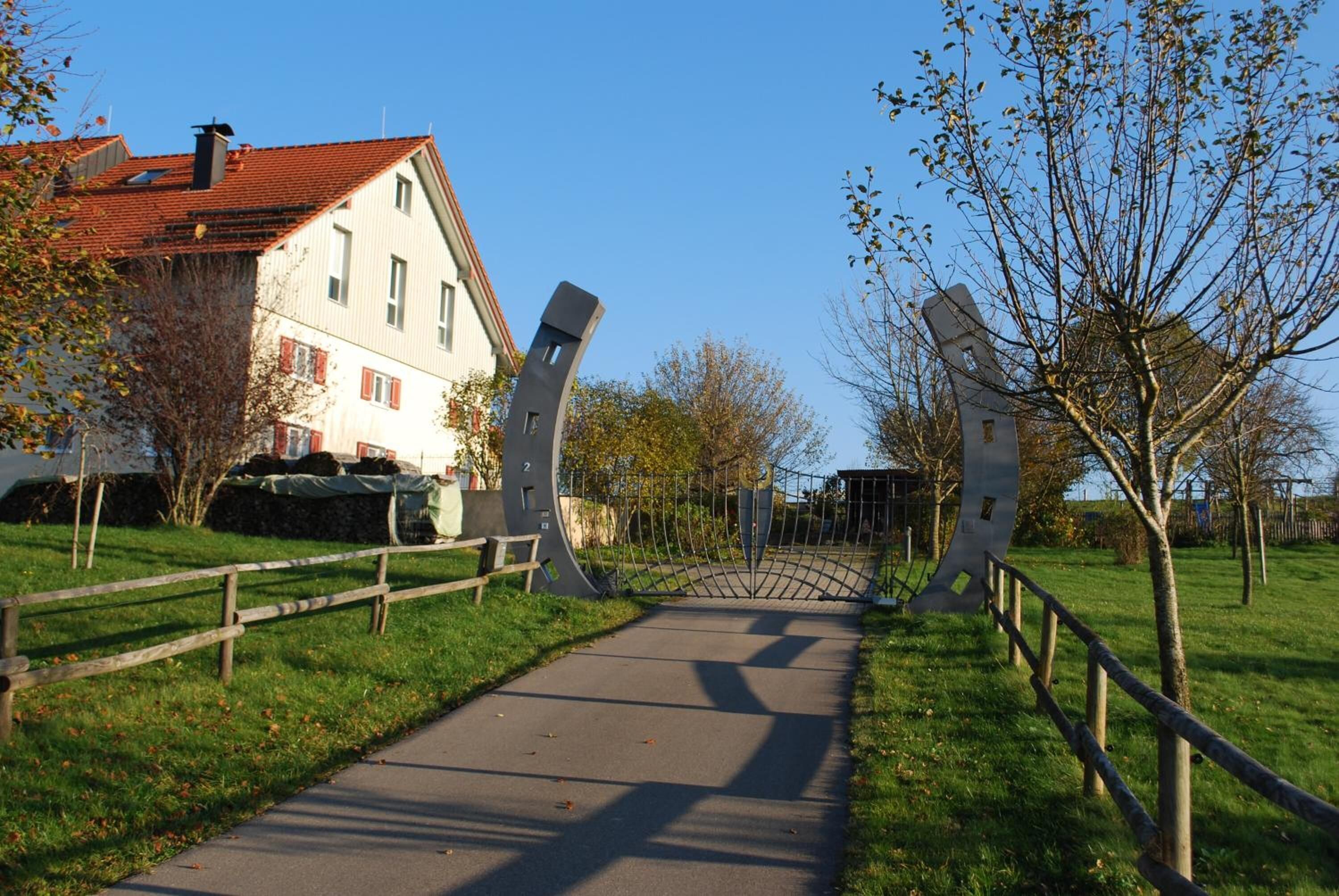 A pathway leading to a building with a red-tiled roof, surrounded by trees and a wooden fence.