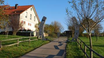 A pathway leading to a building with a red-tiled roof, surrounded by trees and a wooden fence.