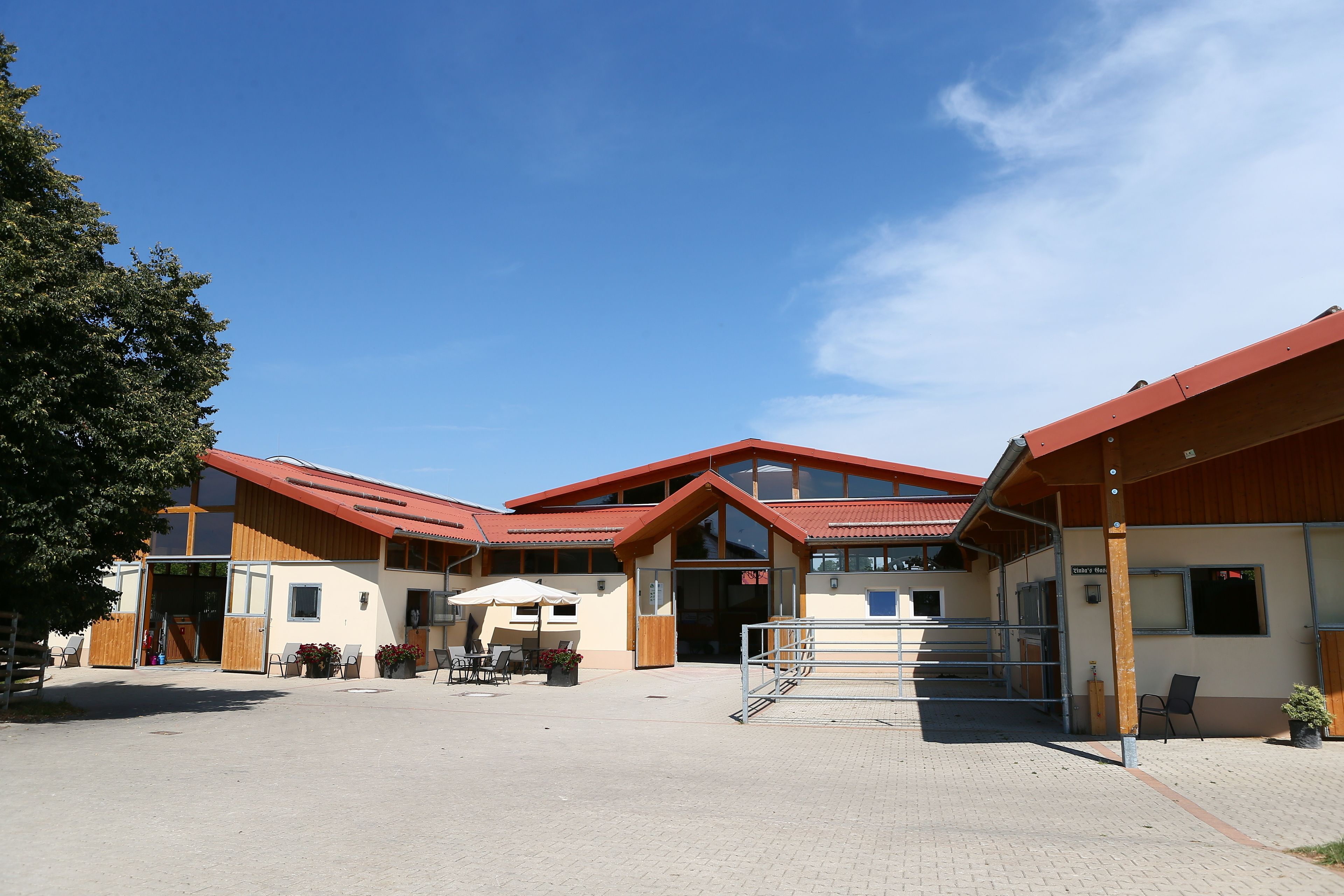 A building with a red roof and a large entrance. There are outdoor seating areas with tables and chairs.