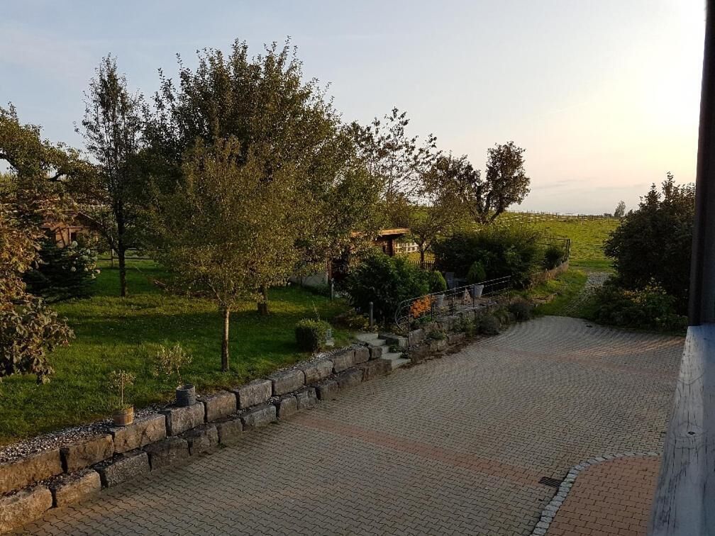 Un camí pavimentat que condueix a un edifici rústic amb un mur de pedra i arbres.