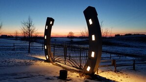 A metal sculpture with illuminated panels in a snowy landscape at dusk.