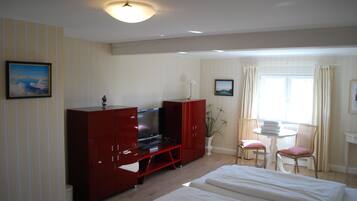 Ein Hotelzimmer mit gestreifter Tapete, einem Fernseher, einem Schreibtisch mit Lampe, zwei Stühlen und einem Bett.