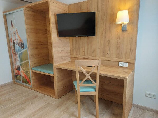 Un escritorio de madera con un televisor montado encima, una silla con cojín verde y una lámpara fijada a la pared.