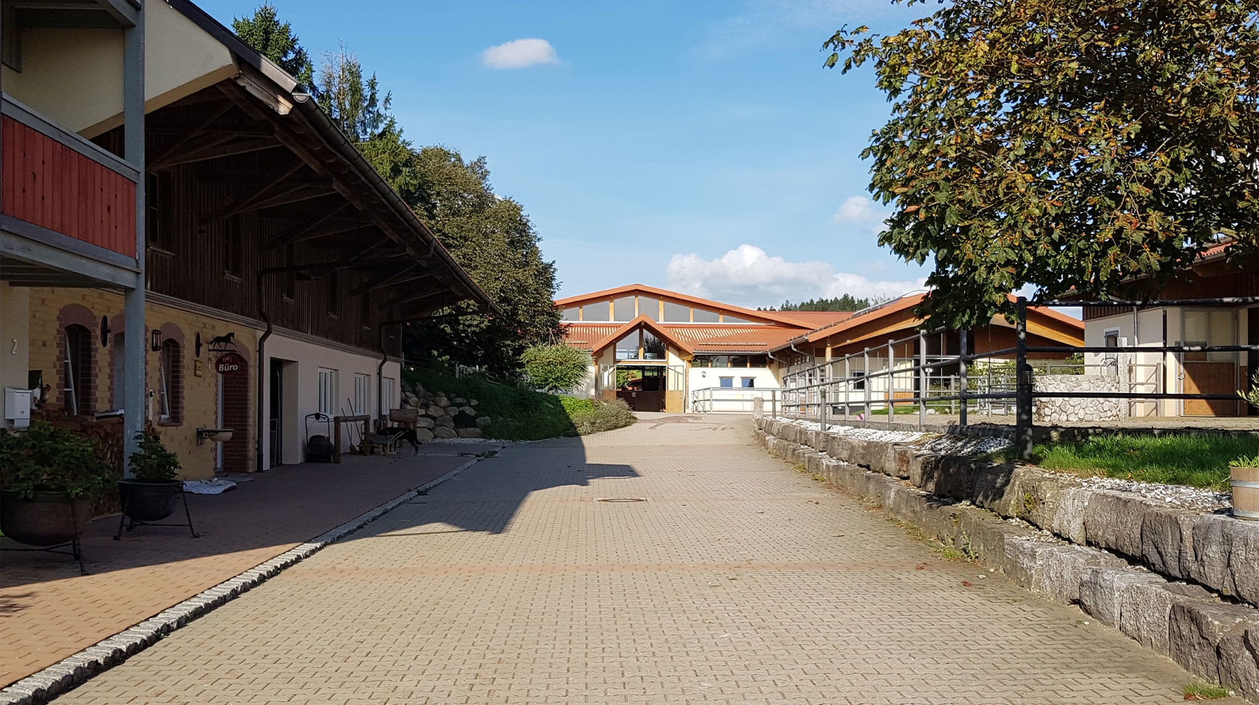 Ein Kopfsteinpflasterweg führt zu einem traditionellen Gebäude mit Holzfassade und rotem Dach.