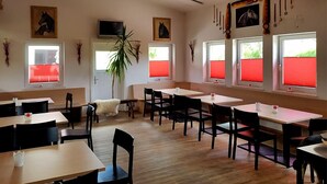Un comedor con varias mesas y sillas, un televisor montado en la pared y persianas rojas.