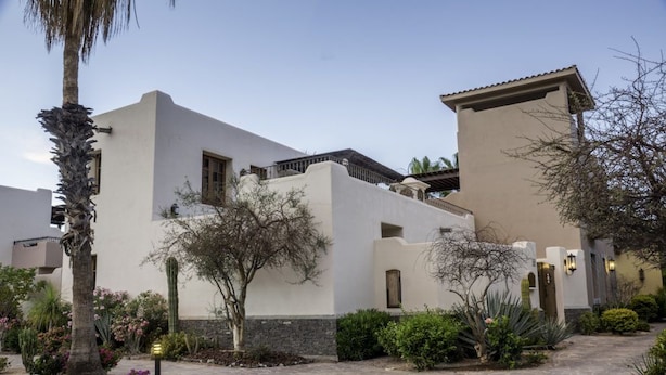 Un bâtiment moderne à la façade blanche, doté d’un toit plat et d’une cour pavée de pierres.