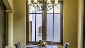 Un coin repas avec une table dressée pour quatre personnes, un lustre et une fenêtre donnant sur un immeuble.