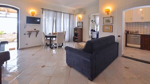 A living room with a sofa, a dining table with chairs, a TV mounted on the wall, and a kitchen area with cabinets and a stove. - Star Fish House (Ravello)