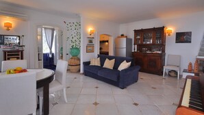 A living room with a blue sofa, a dining table with chairs, a piano, and a kitchen area in the background. - Star Fish House (Ravello)