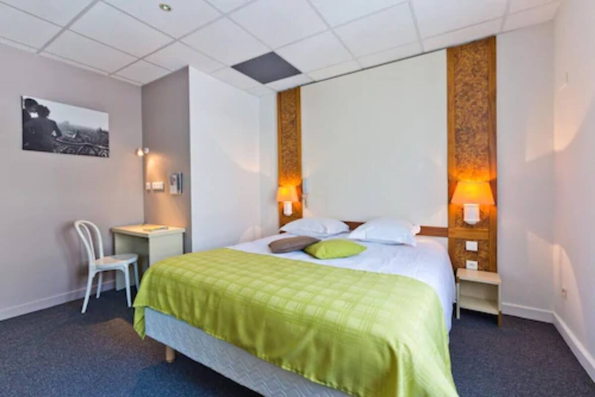 Una habitación de hotel con cama, escritorio, silla y un cuadro en la pared.