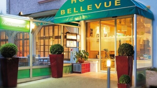 Ein Hotel namens "Hotel Bellevue" mit einer grünen Markise, großen Fenstern und Blumentöpfen vor der Fassade.